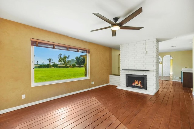 unfurnished living room featuring a brick fireplace, wood-type flooring, and ceiling fan