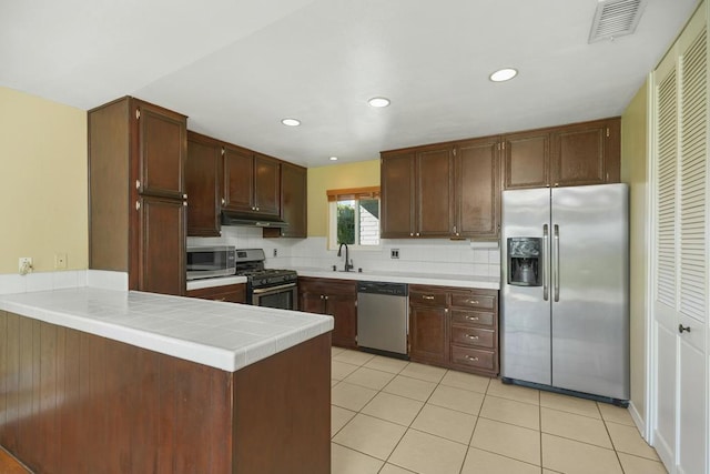 kitchen with sink, light tile patterned floors, stainless steel appliances, tasteful backsplash, and kitchen peninsula