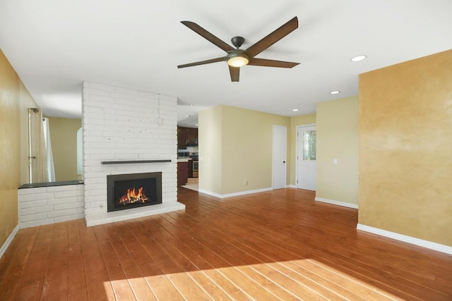 unfurnished living room with ceiling fan, a fireplace, and wood-type flooring