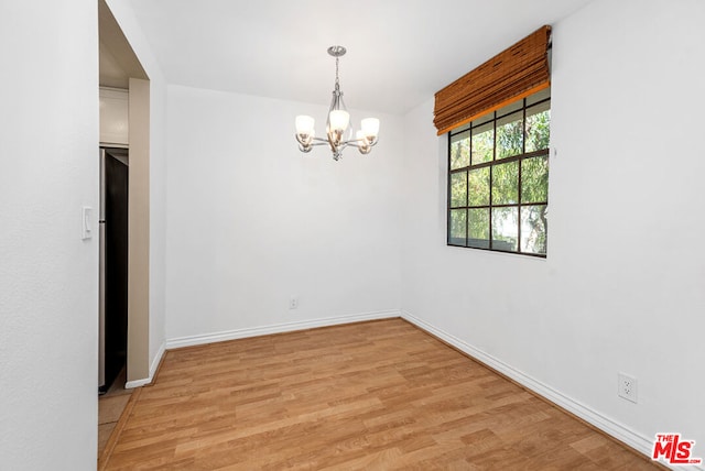 unfurnished room featuring an inviting chandelier and light hardwood / wood-style flooring