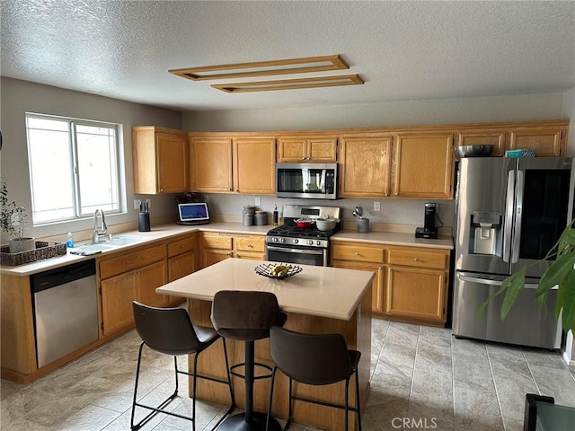 kitchen with a textured ceiling, stainless steel appliances, sink, a center island, and a breakfast bar area