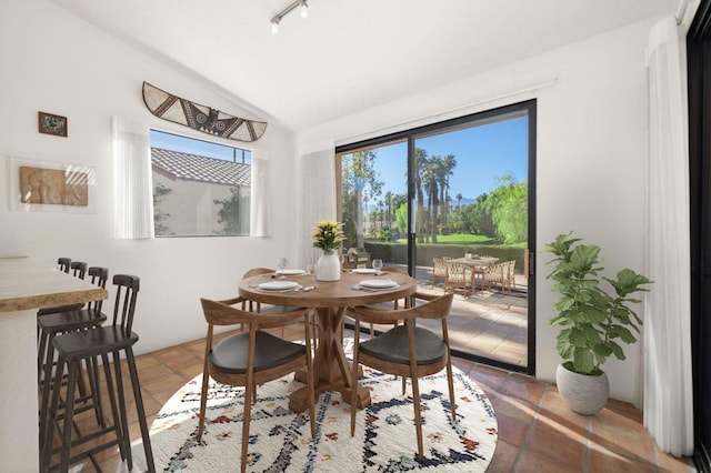 dining space featuring tile patterned flooring, rail lighting, and vaulted ceiling