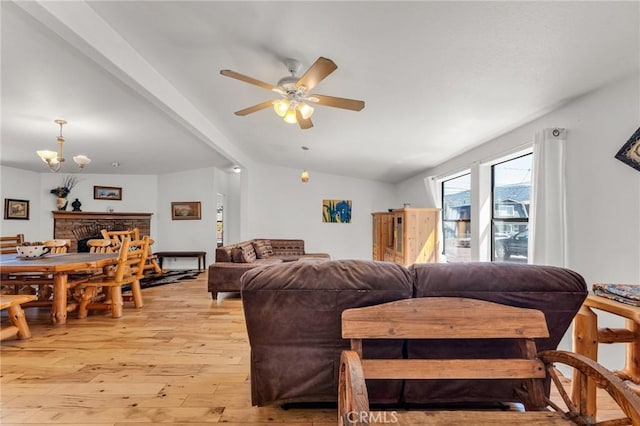 living room featuring ceiling fan with notable chandelier, light wood-type flooring, a fireplace, and lofted ceiling