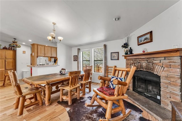 dining area featuring a fireplace, light hardwood / wood-style floors, vaulted ceiling, and a notable chandelier