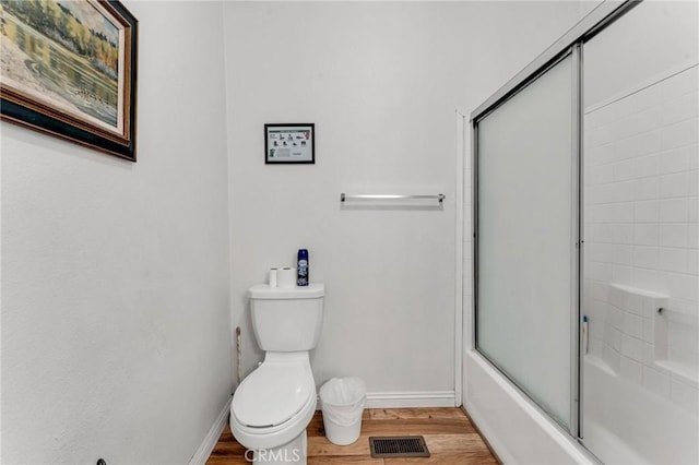 bathroom with hardwood / wood-style flooring, toilet, and enclosed tub / shower combo