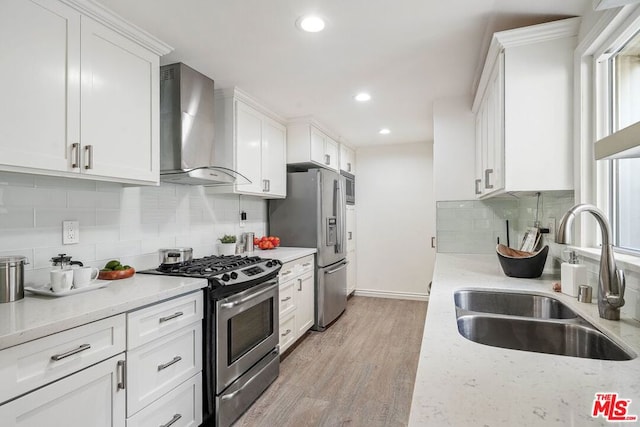 kitchen with sink, wall chimney exhaust hood, appliances with stainless steel finishes, white cabinets, and light wood-type flooring