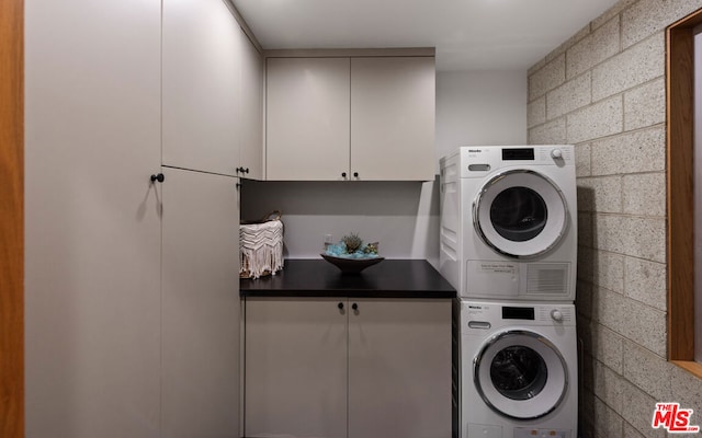 laundry room featuring cabinets and stacked washer / dryer