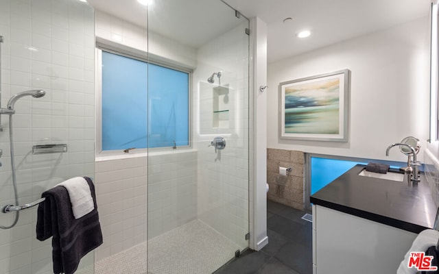 bathroom with tile patterned floors, toilet, vanity, a shower with shower door, and tile walls