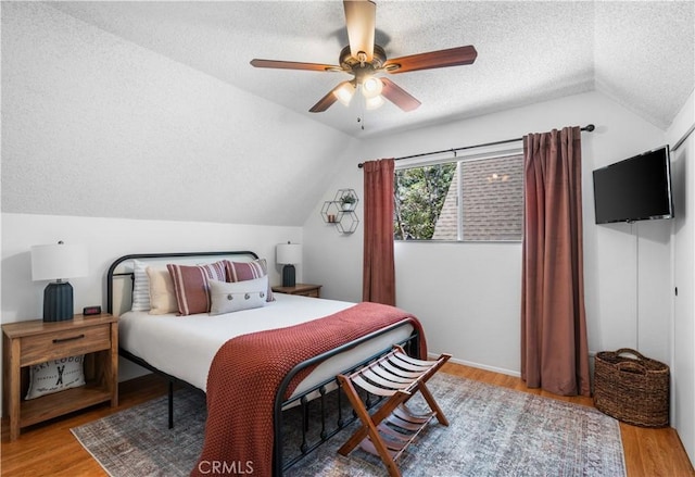 bedroom featuring a textured ceiling, light hardwood / wood-style floors, vaulted ceiling, and ceiling fan