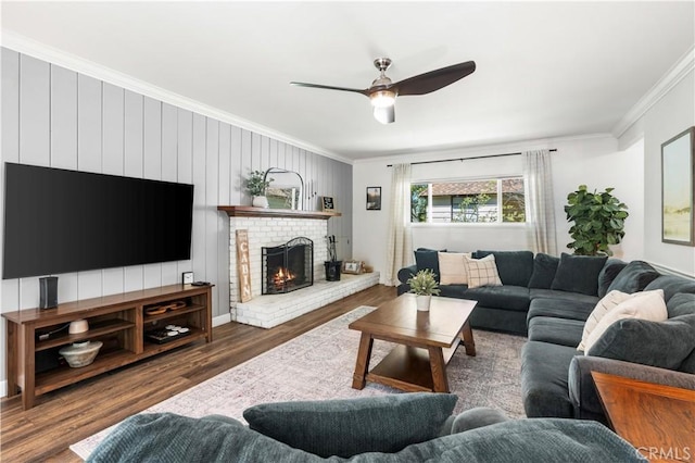 living room with a brick fireplace, ceiling fan, crown molding, and dark wood-type flooring