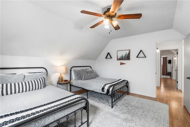 bedroom with a textured ceiling, ceiling fan, light hardwood / wood-style floors, and lofted ceiling