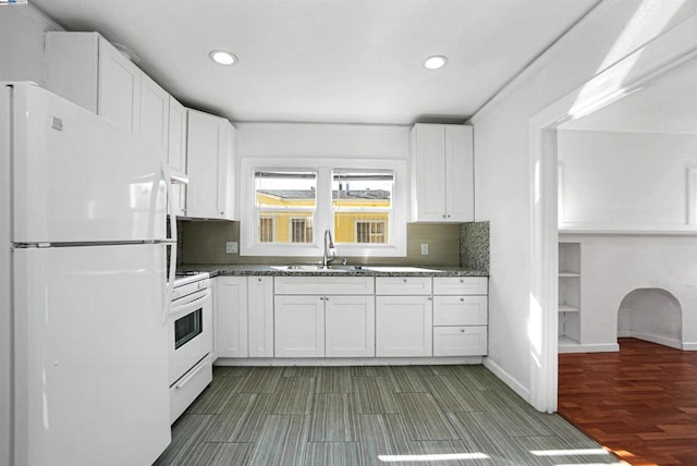 kitchen featuring white appliances, dark stone countertops, decorative backsplash, white cabinets, and sink