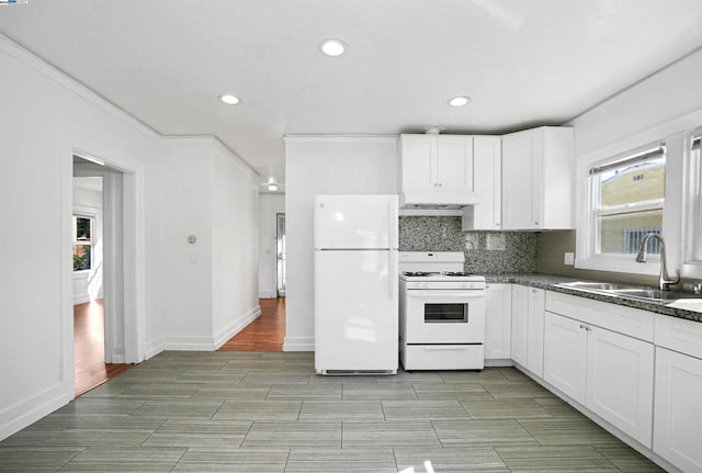 kitchen featuring white appliances, decorative backsplash, white cabinets, dark stone countertops, and sink