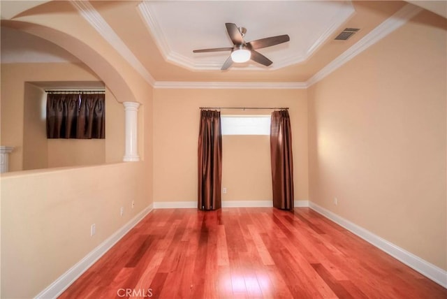 empty room featuring decorative columns, a tray ceiling, ceiling fan, crown molding, and hardwood / wood-style flooring