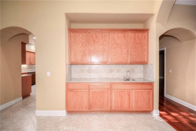 kitchen featuring decorative backsplash, light brown cabinetry, stainless steel dishwasher, and light hardwood / wood-style floors