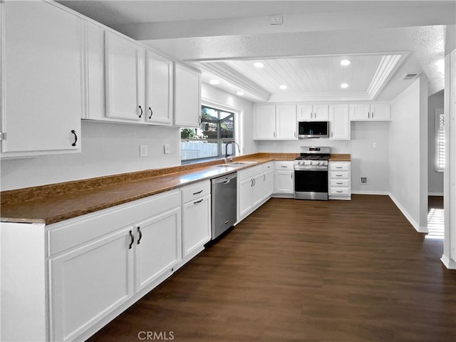 kitchen with appliances with stainless steel finishes, a tray ceiling, dark wood-type flooring, sink, and white cabinets