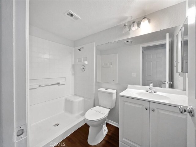 bathroom featuring a tile shower, vanity, a textured ceiling, hardwood / wood-style flooring, and toilet