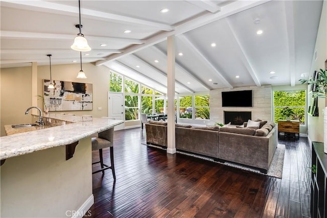 living room featuring vaulted ceiling with beams, sink, dark wood-type flooring, and a fireplace