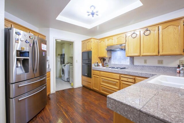 kitchen with dark hardwood / wood-style floors, sink, black appliances, a raised ceiling, and washing machine and dryer