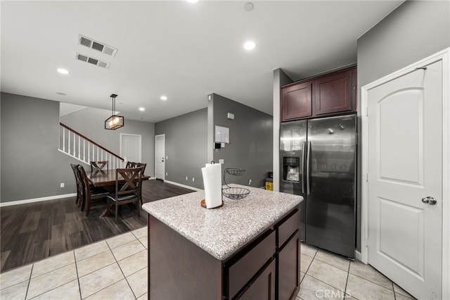 kitchen with hanging light fixtures, light hardwood / wood-style flooring, stainless steel fridge, dark brown cabinets, and a kitchen island