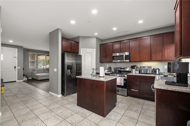 kitchen featuring light stone countertops, appliances with stainless steel finishes, a center island, and light tile patterned floors