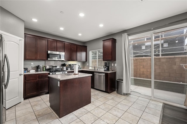 kitchen featuring appliances with stainless steel finishes, dark brown cabinets, sink, light tile patterned floors, and a kitchen island