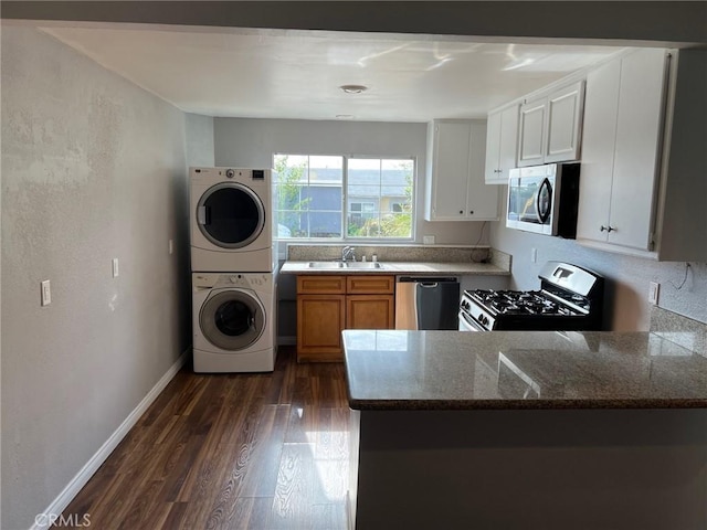 kitchen with white cabinetry, sink, stacked washing maching and dryer, dark hardwood / wood-style flooring, and appliances with stainless steel finishes