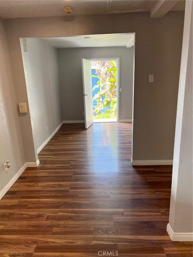 empty room featuring beamed ceiling and dark wood-type flooring