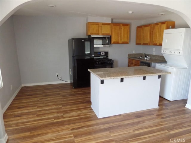 kitchen with black appliances, a kitchen breakfast bar, a center island, and stacked washer and dryer