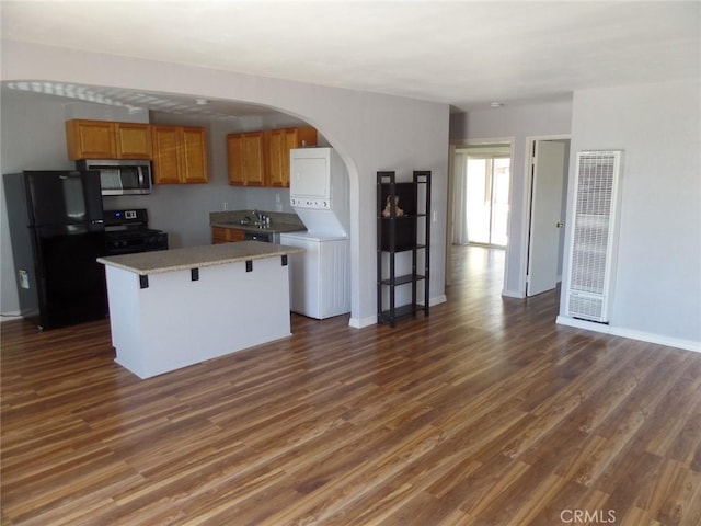 kitchen featuring a breakfast bar, a center island, dark wood-type flooring, black appliances, and stacked washer / dryer