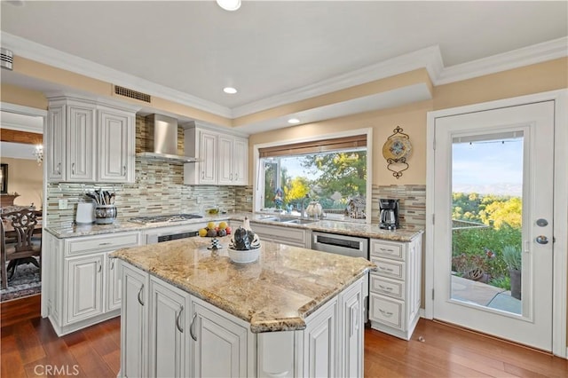 kitchen featuring decorative backsplash, wall chimney range hood, white cabinetry, and a kitchen island