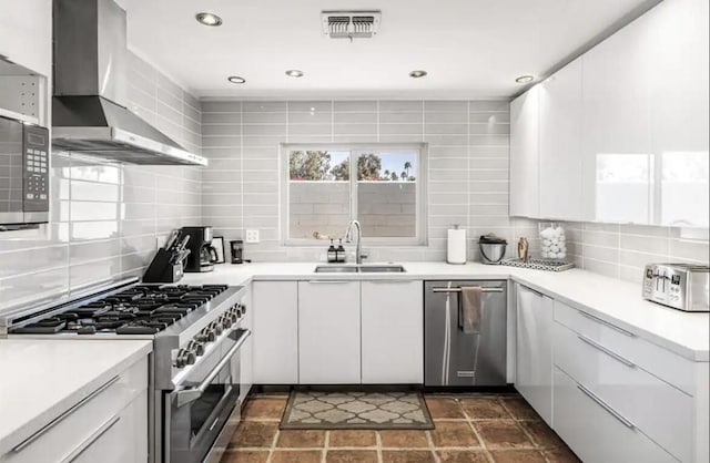 kitchen featuring white cabinetry, wall chimney range hood, sink, and appliances with stainless steel finishes