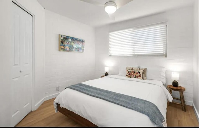 bedroom featuring a closet, light hardwood / wood-style floors, ceiling fan, and brick wall