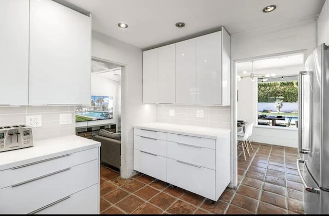 kitchen with stainless steel fridge, white cabinetry, and backsplash