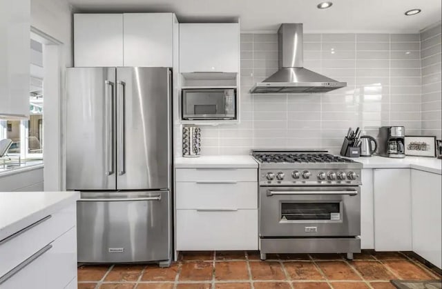 kitchen featuring wall chimney exhaust hood, premium appliances, decorative backsplash, and white cabinetry