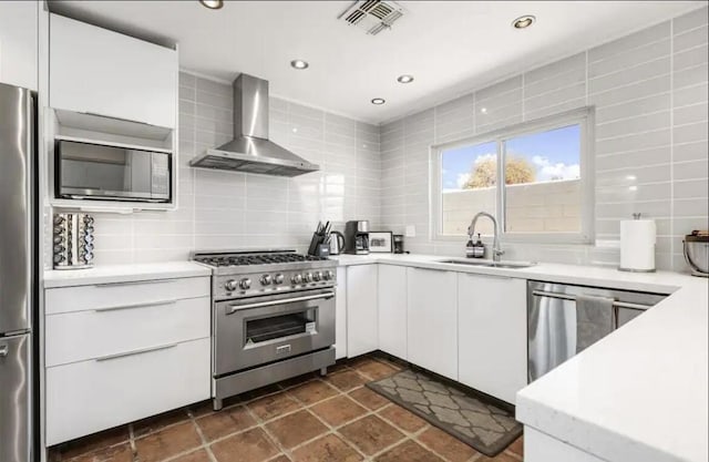 kitchen with sink, wall chimney exhaust hood, decorative backsplash, appliances with stainless steel finishes, and white cabinetry