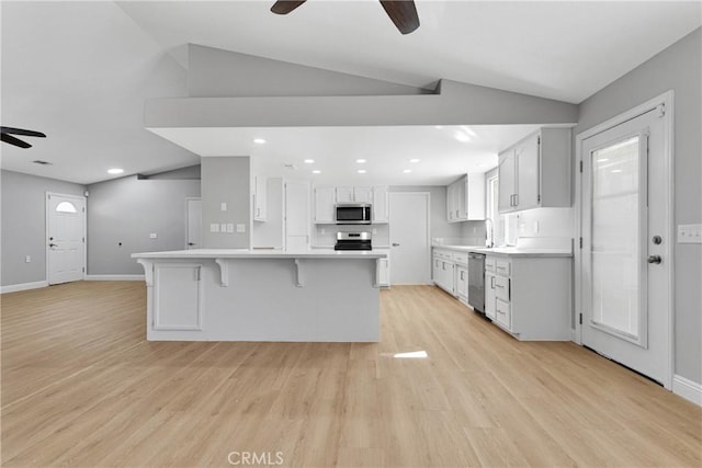 kitchen with appliances with stainless steel finishes, vaulted ceiling, light hardwood / wood-style flooring, a center island, and white cabinetry