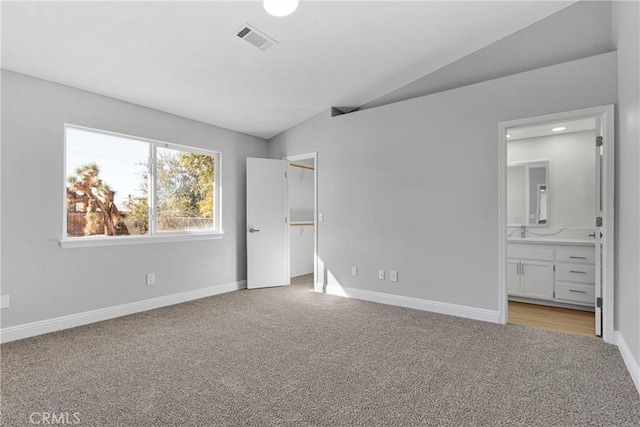 unfurnished bedroom featuring sink, light carpet, connected bathroom, and vaulted ceiling