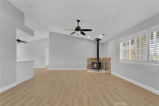 unfurnished living room featuring ceiling fan, vaulted ceiling, a wood stove, and light hardwood / wood-style flooring