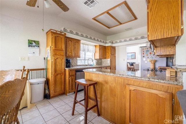 kitchen with light stone countertops, dishwasher, kitchen peninsula, decorative backsplash, and a breakfast bar