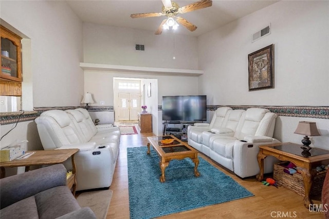 living room featuring a high ceiling, light wood-type flooring, and ceiling fan