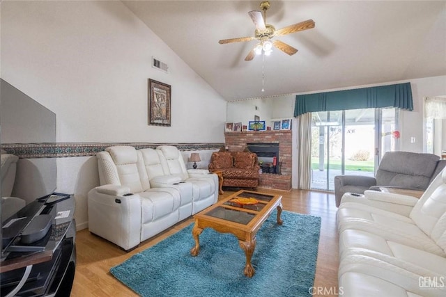 living room featuring a brick fireplace, light hardwood / wood-style flooring, vaulted ceiling, and ceiling fan