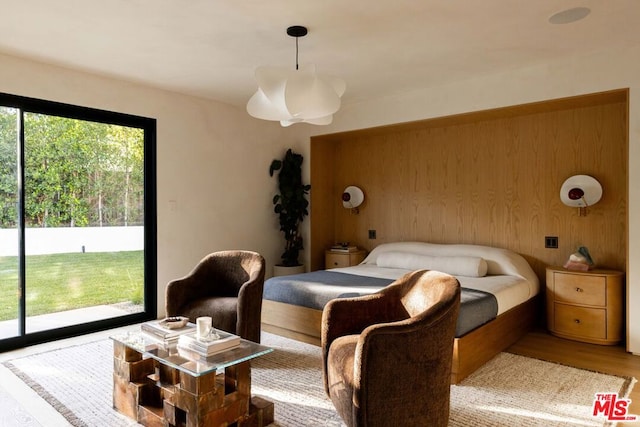 bedroom with access to outside, light hardwood / wood-style floors, and wood walls