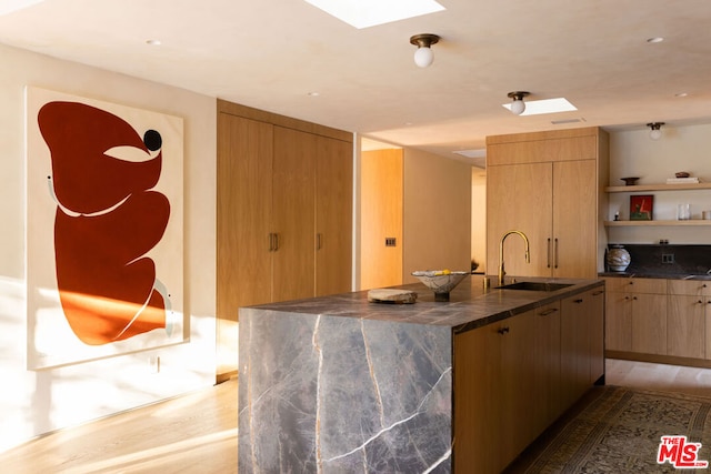 kitchen with a skylight, sink, light brown cabinets, light hardwood / wood-style flooring, and a kitchen island with sink