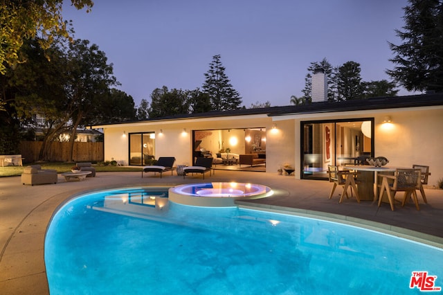 pool at dusk featuring an in ground hot tub, a patio, and an outdoor hangout area