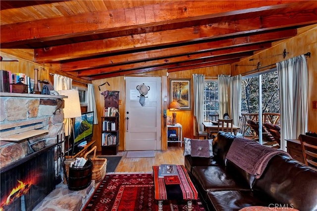 living room with light wood-type flooring, vaulted ceiling with beams, a stone fireplace, and wood walls