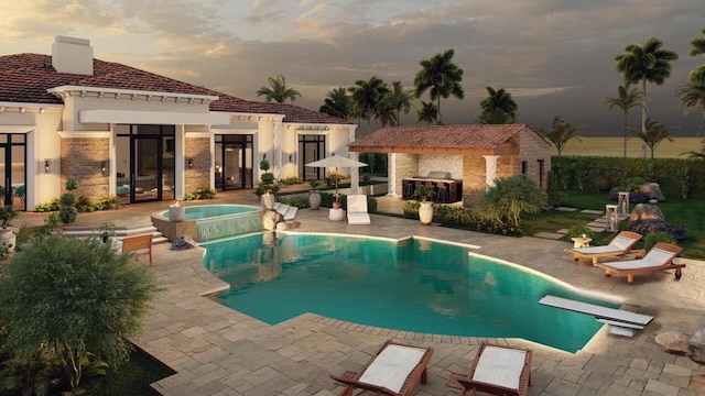 pool at dusk featuring a diving board, a patio area, an in ground hot tub, and an outbuilding