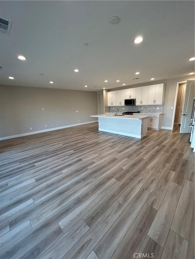 kitchen featuring white cabinetry, backsplash, a kitchen island with sink, light hardwood / wood-style flooring, and sink