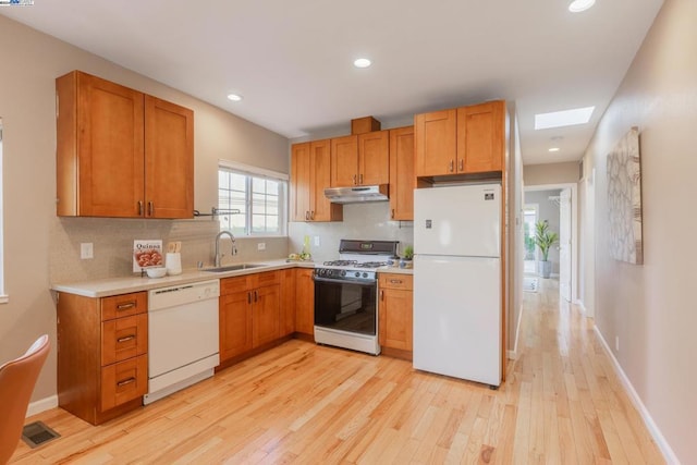 kitchen featuring white appliances, sink, a skylight, tasteful backsplash, and light hardwood / wood-style floors