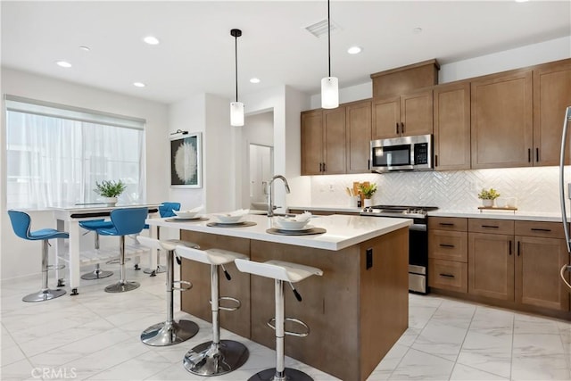 kitchen with sink, pendant lighting, a kitchen bar, a kitchen island with sink, and appliances with stainless steel finishes